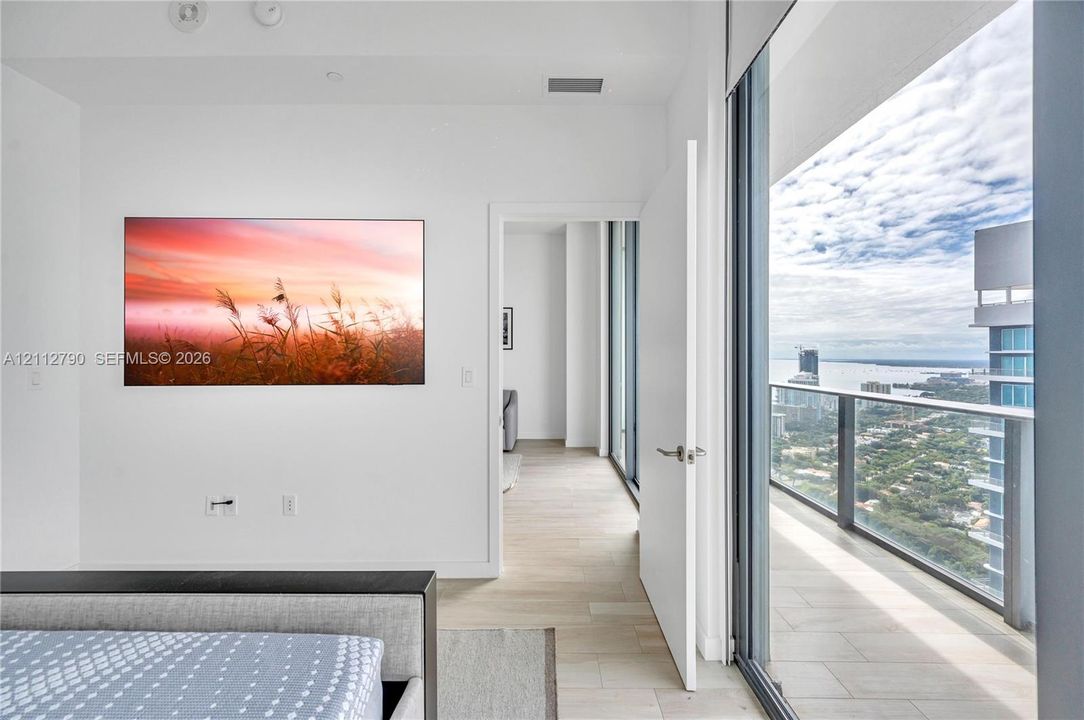 Floor-to-ceiling glass door, private balcony with glass railing, wood-finish flooring, and expansive exterior coastal scenery
