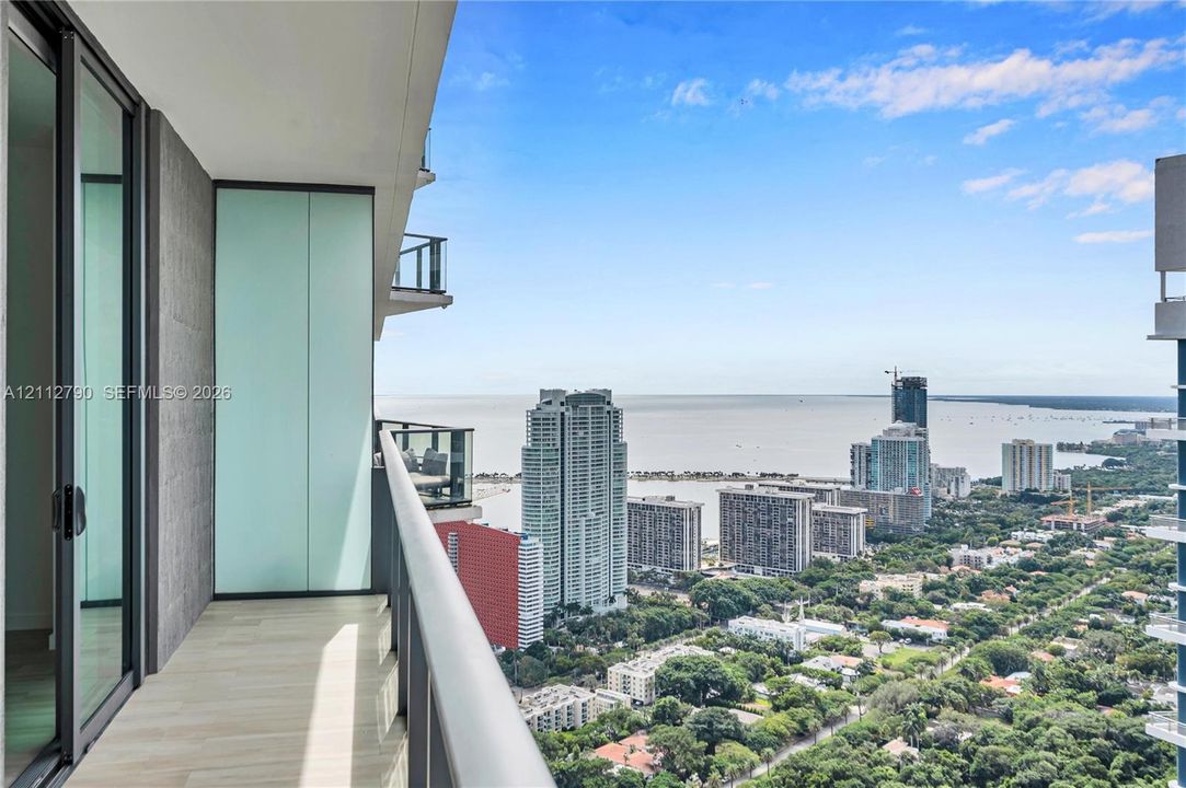 Covered balcony featuring wood-finish flooring, glass-panel railings, and expansive water and urban scenery