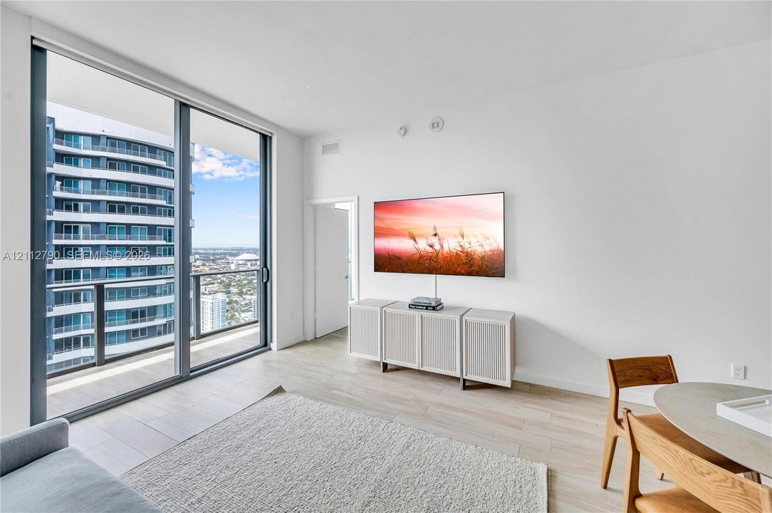 Floor-to-ceiling glass sliding doors, wood-finish flooring, and an expansive balcony