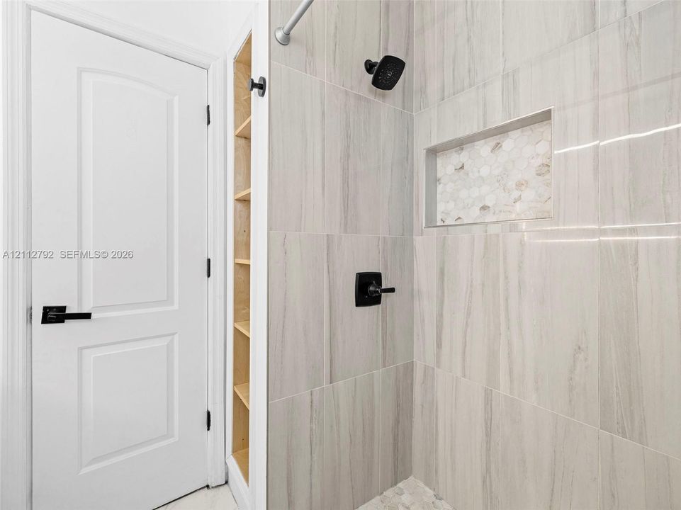Shower enclosure featuring large-format tile walls, a built-in recessed niche with mosaic accent tile, matte black fixtures, and a recessed storage shelf