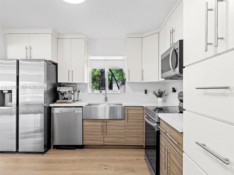 Kitchen featuring white upper cabinetry, wood-finish lower cabinetry, stainless steel apron-front sink, white countertops, and stainless steel appliances