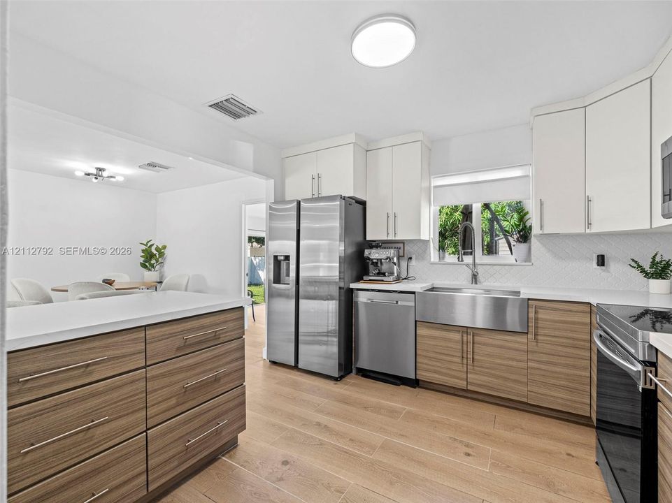 Kitchen featuring wood-finish cabinetry with flat-panel doors, quartz countertops, stainless steel farmhouse sink, wood-finish flooring, and stainless steel appliances