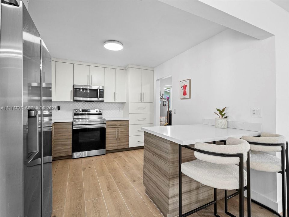 Kitchen featuring two-tone flat-panel cabinetry, stainless steel appliances, wood-finish flooring, and a built-in island with a solid-surface countertop