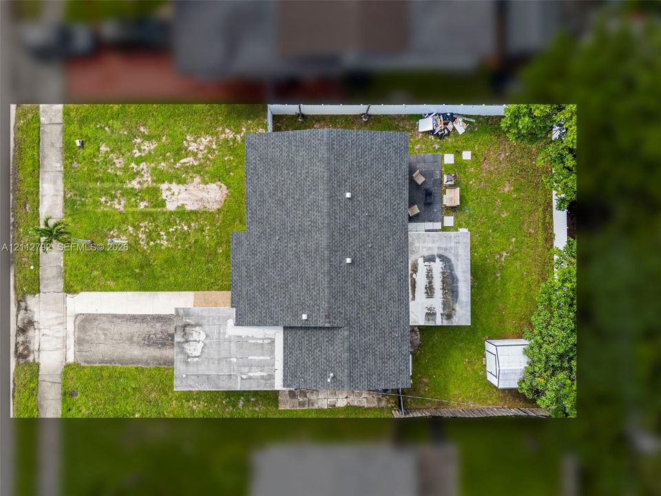 Aerial view of property featuring a composite shingle roof, concrete driveway, paved patio, and detached storage structure
