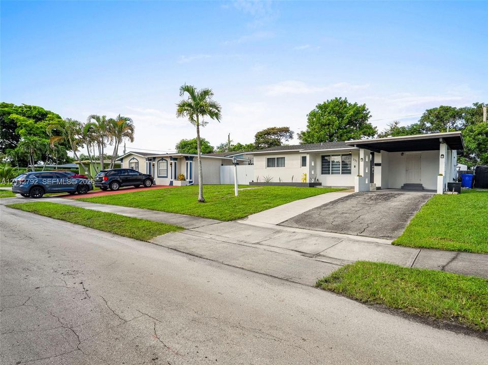 Single-story exterior featuring painted brick masonry, an integrated carport, a concrete driveway, and mature palm landscaping