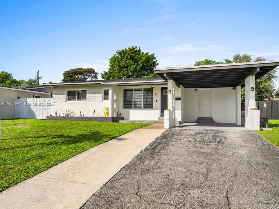 Single-story exterior with a painted masonry finish, attached carport, concrete driveway, and front lawn