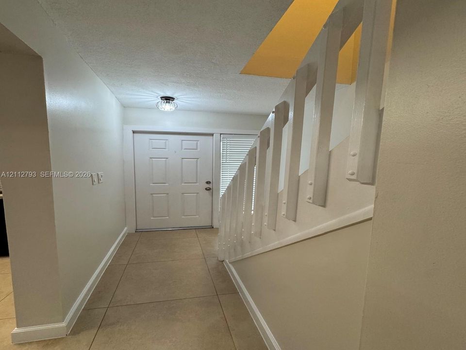 Entryway featuring large-format tile flooring, a paneled front door, white balustrade staircase, and flush-mount ceiling lighting