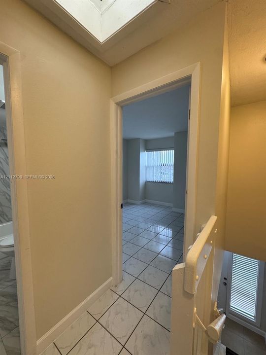 Interior hall featuring tile flooring with marble-pattern detail, skylight, and doorway access to multiple rooms