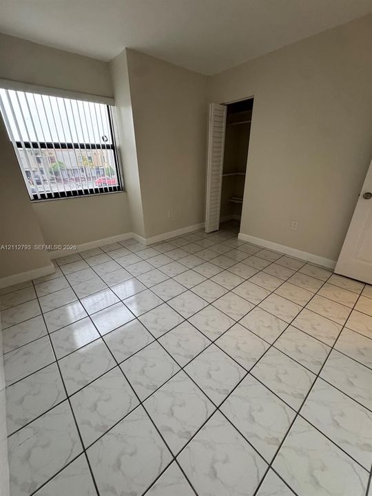 Room featuring large-format diagonal tile flooring, neutral wall paint, a window with vertical blinds, and a built-in closet with louvered doors