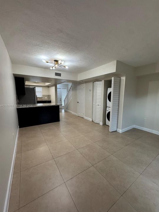 kitchen featuring dark cabinetry and stone-finish countertops, multi-arm flush mount lighting, and laundry closet with stacked unit