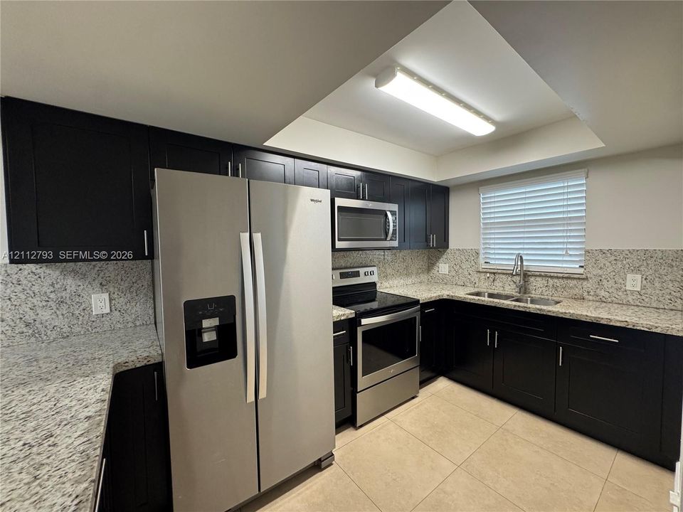 Kitchen featuring dark cabinetry, stone-finish countertops, stainless steel appliances, dual-basin sink, and tile flooring
