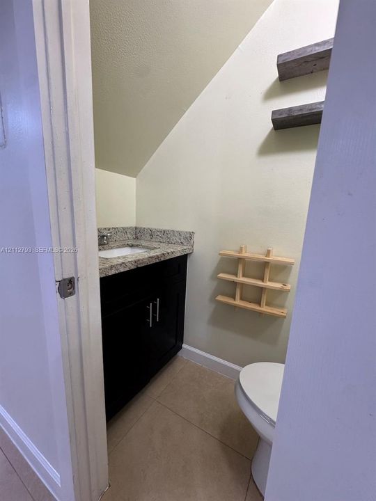 Dark-finish vanity cabinetry with stone-surface countertop, rectangular undermount sink, and neutral tile flooring