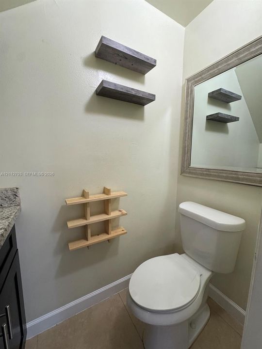 Vanity featuring a stone countertop, wall-mounted wood-finish shelving, and a framed wall mirror