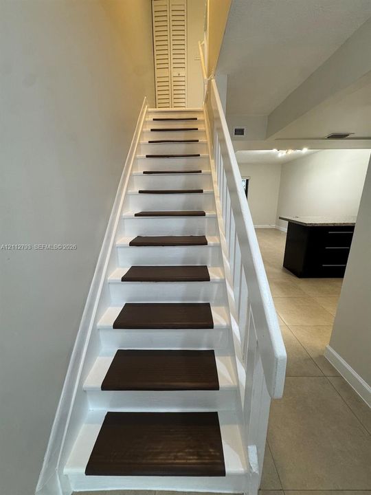 Staircase featuring white risers and handrail with dark tread inserts, complemented by neutral tile flooring and built-in louvered closet doors