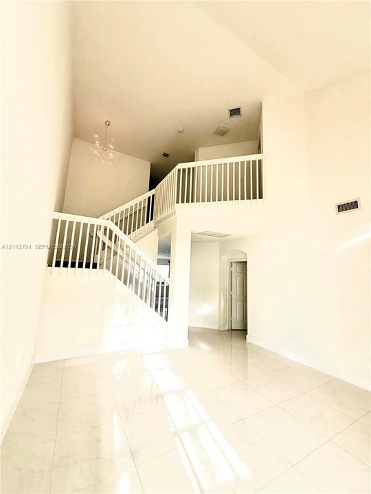Two-story foyer featuring high ceilings, large-format tile flooring, a multi-tiered staircase with white balusters, and a decorative chandelier