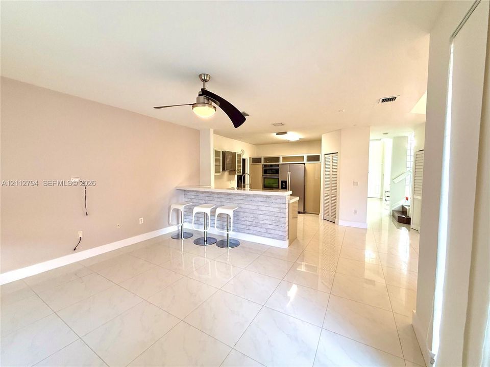 Open-concept interior featuring large-format tile flooring, a breakfast bar with stone-finish cladding, built-in stainless steel appliances, and a ceiling-mounted light fixture