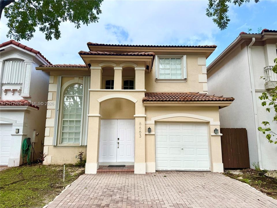 Two-story stucco exterior featuring a barrel-tile roof, arched entryway with decorative columns, double-door entrance, and a paved driveway