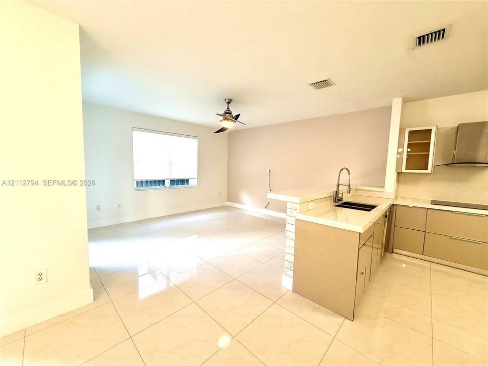Kitchen featuring sleek flat-panel cabinetry, quartz countertops, a stainless steel undermount sink with a gooseneck faucet, and stainless steel range hood, complemented by large-format tile flooring throughout