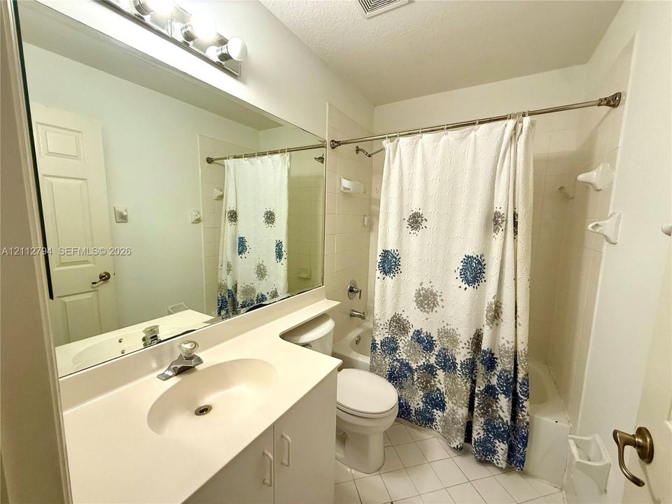 Full-width wall mirror, white vanity cabinet with an integrated sink, polished chrome faucet, tile surround tub and shower combination, and tile flooring