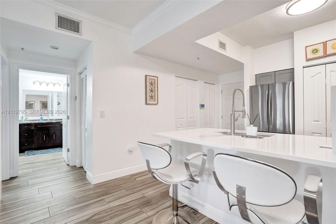 Kitchen featuring a breakfast bar with a solid surface countertop, stainless steel refrigerator, pull-down chrome faucet, and wood-finish flooring