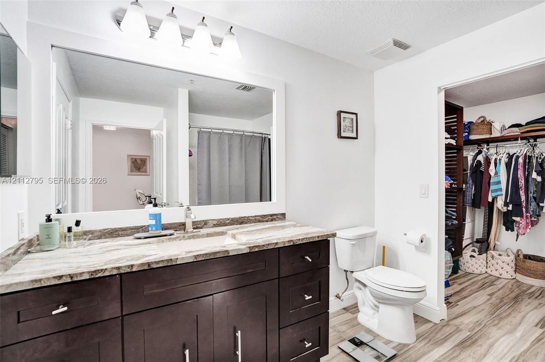 Bathroom featuring a dark-finish vanity with stone-patterned countertop, large wall-mounted mirror, overhead multi-light fixture, and wood-finish flooring
