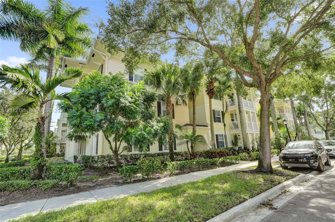 Multi-story exterior featuring pale yellow siding, shuttered windows, covered balconies, and mature palm and oak landscaping