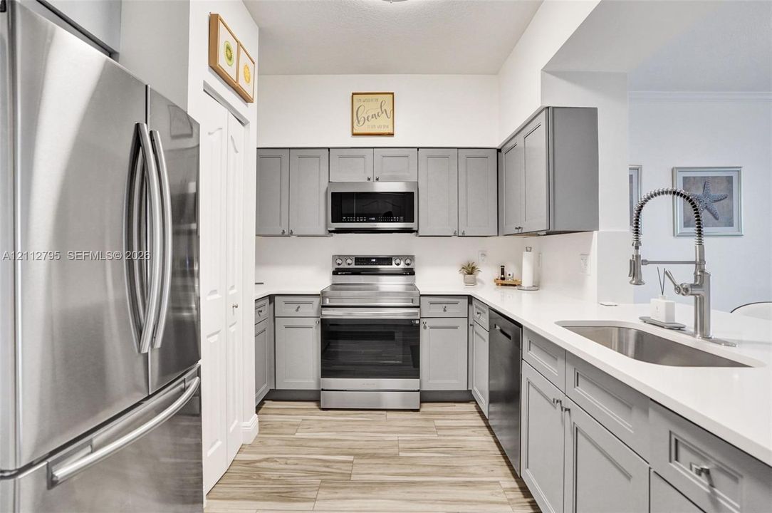 Kitchen featuring grey shaker-style cabinetry, stainless steel appliances, solid surface countertops, wood-finish tile flooring, and a gooseneck faucet