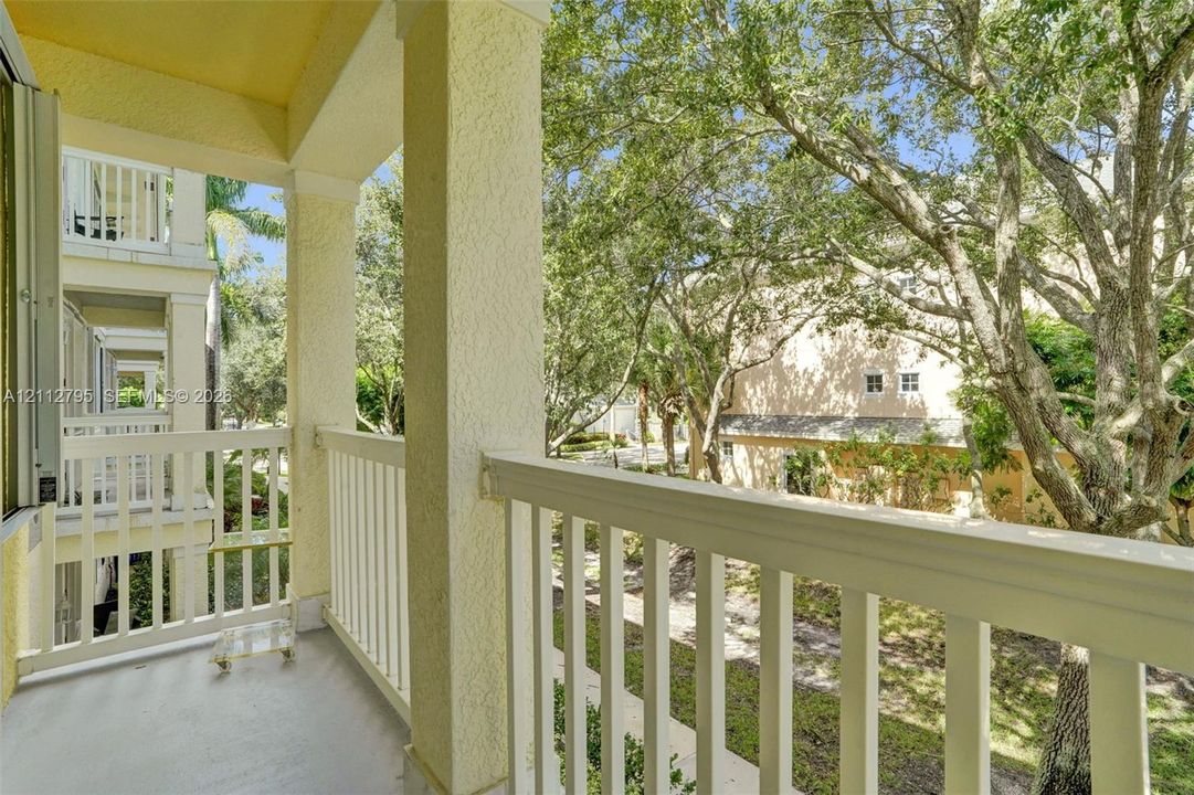 Covered balcony featuring white vertical railings, stucco-finished support columns, and mature canopy trees