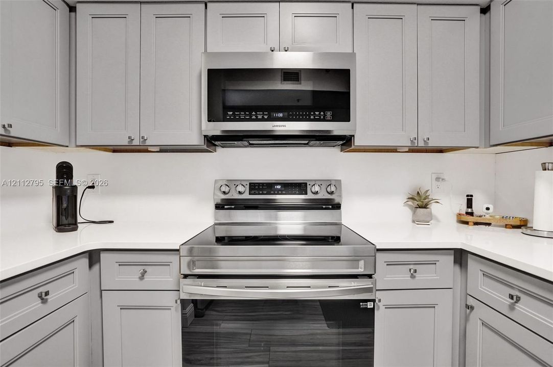 Kitchen featuring grey shaker-style cabinetry, solid-surface countertops, and stainless steel appliances, including an over-the-range microwave and a smooth-top range