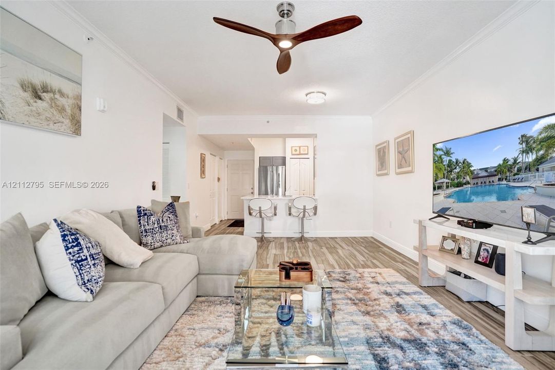 Open-concept room featuring wood-finish flooring, a contemporary three-blade ceiling fan, and crown molding