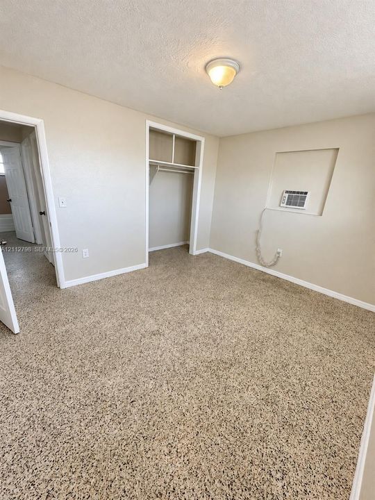 Interior room featuring textured carpeting, a built-in closet with overhead shelving, a recessed wall niche, and a flush-mount ceiling light fixture
