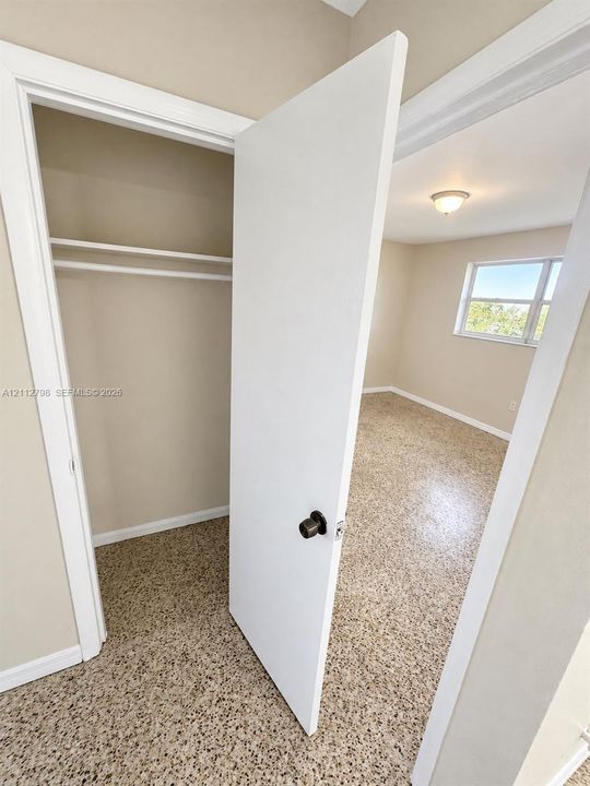 Interior room featuring speckled composition flooring, neutral wall paint, a window, built-in closet shelving, and a flush-mount ceiling light fixture