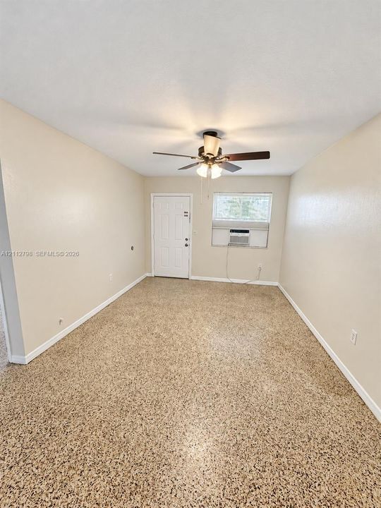 Neutral-toned interior space featuring speckled composition flooring, a central ceiling fan with integrated light fixture, a paneled entry door, and an operable window