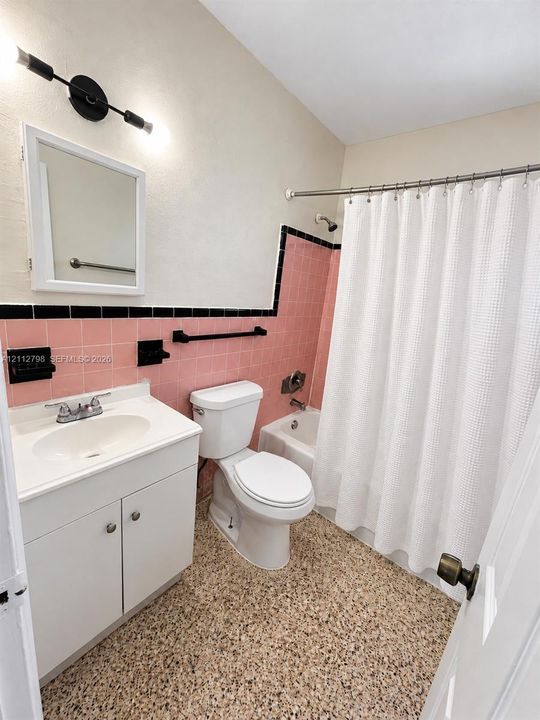 Bathroom featuring a white vanity cabinet, pink ceramic wall tiling with black trim, a tub-shower combination, and speckled stone-finish flooring