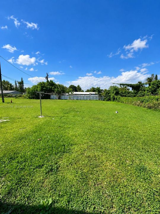 Expansive grass-covered lot featuring perimeter vegetation and a metal fence