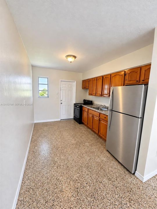 Kitchen featuring wood cabinetry, stone-finish countertops, stainless steel refrigerator, neutral flooring, and a six-panel door