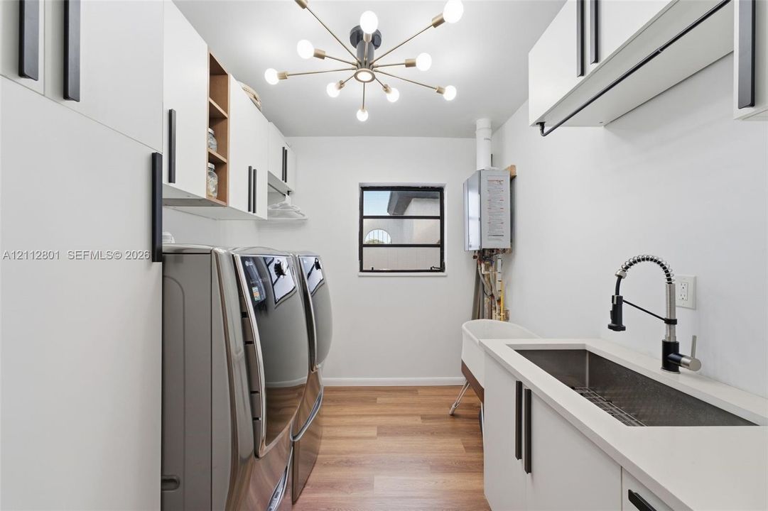 Laundry room featuring white cabinetry with matte black hardware, wood-finish flooring, quartz countertops, a stainless steel undermount sink with a gooseneck faucet, and a multi-arm sputnik-style light fixture