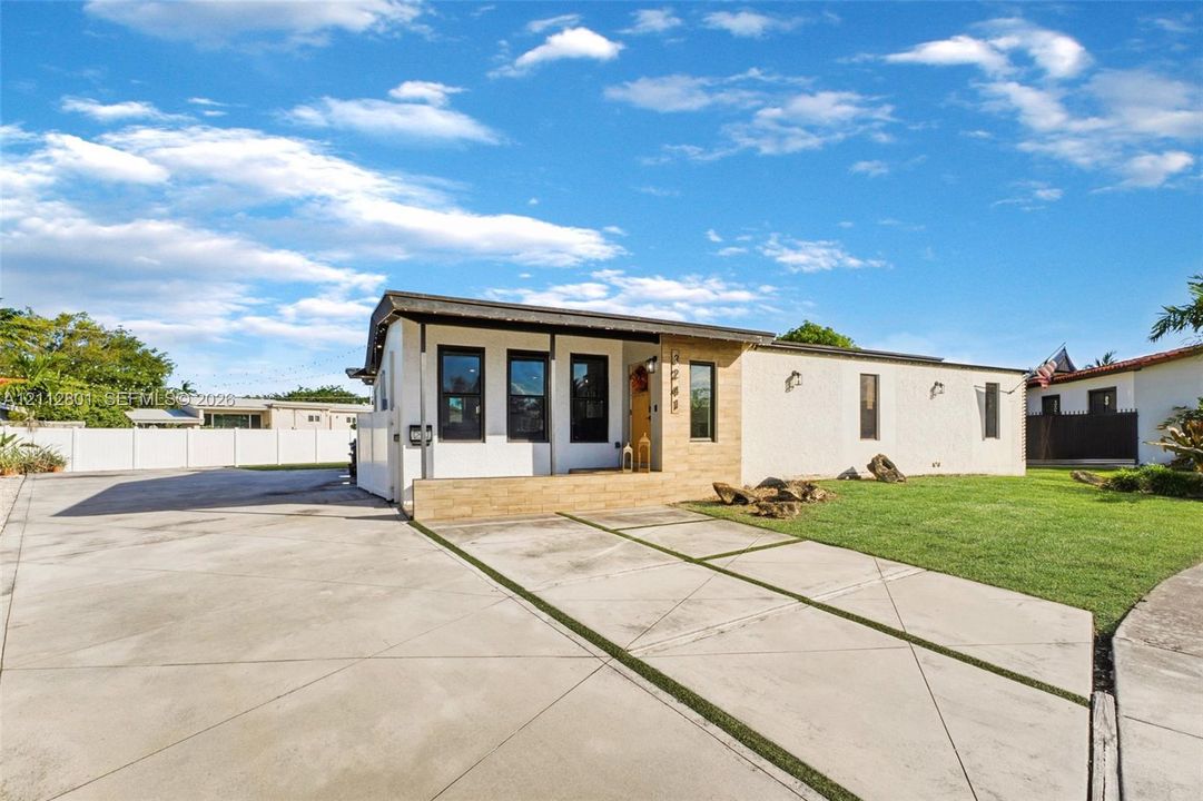 Single-story exterior featuring a stone-accented facade, covered entryway, concrete driveway with integrated turf strips, and perimeter privacy fencing