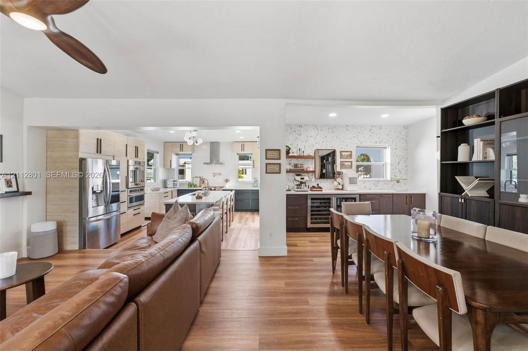 Kitchen featuring stainless steel appliances, a center island with pendant lighting, wood-finish flooring, built-in dark wood shelving, and a wine refrigerator