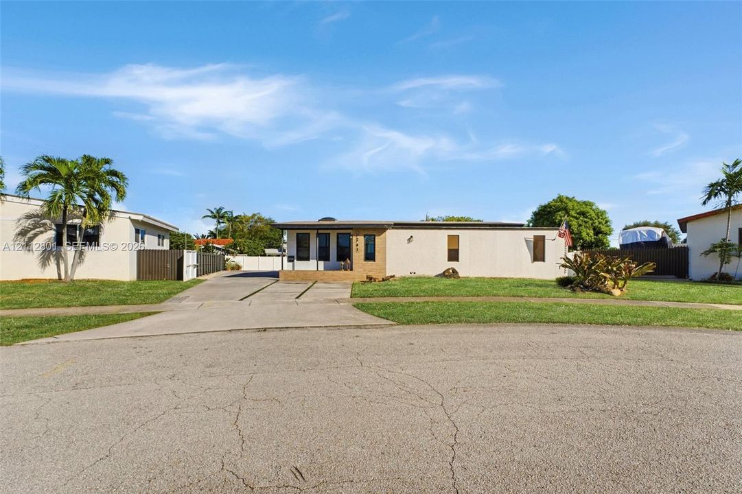Single-story exterior featuring a light-toned stucco facade, concrete driveway, masonry retaining wall, and landscaping