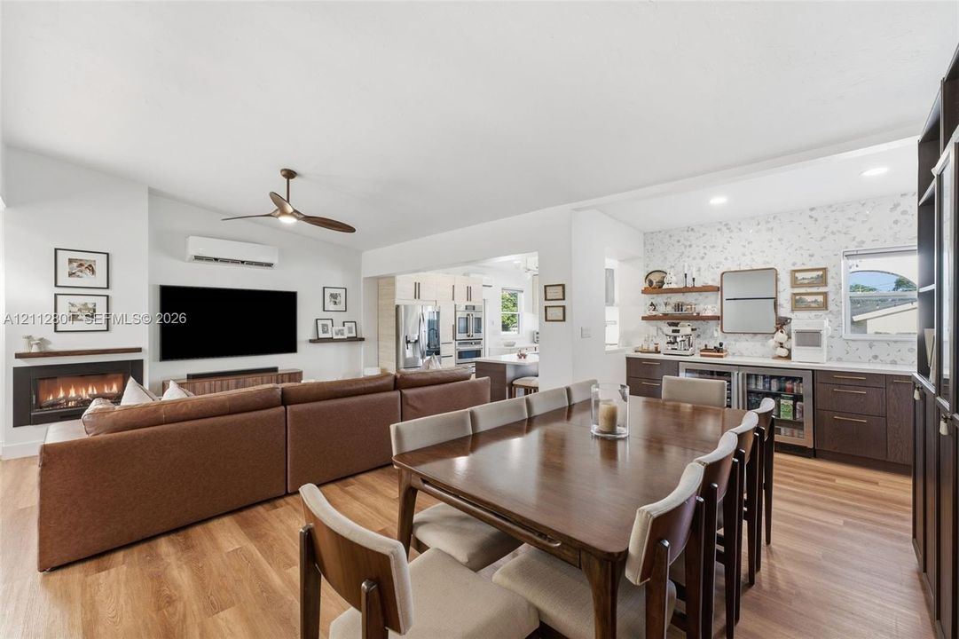 Open-concept living space featuring wood-finish flooring, a wall-mounted linear fireplace with a floating mantel, a ceiling fan, recessed lighting, and a built-in wet bar with dark cabinetry