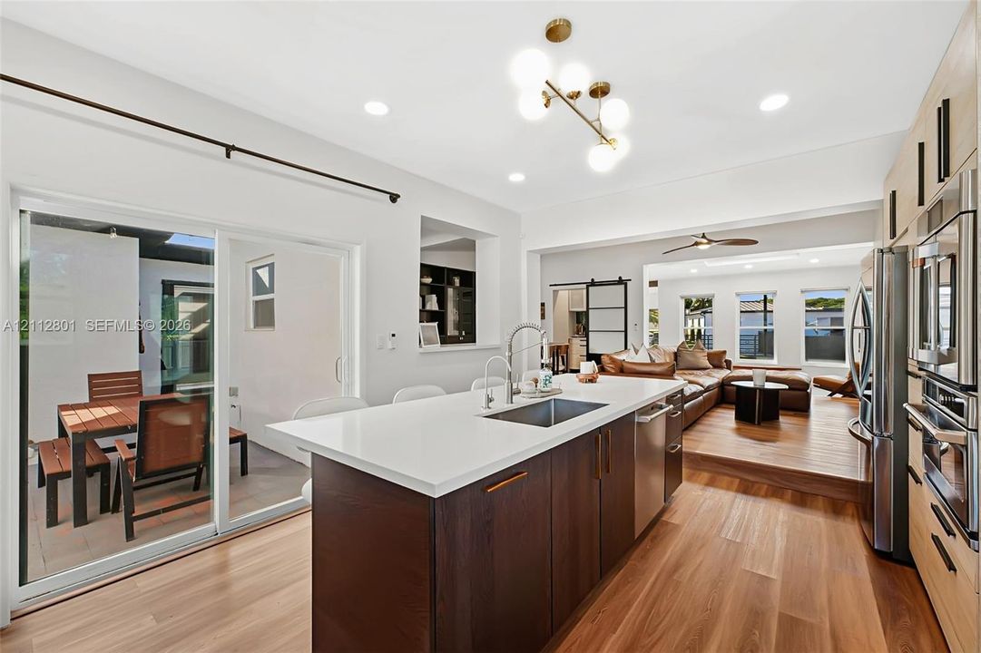 Kitchen featuring a central island with a solid-surface countertop and undermount sink, dark-finish cabinetry, stainless steel appliances, wood-finish flooring, and a multi-globe light fixture