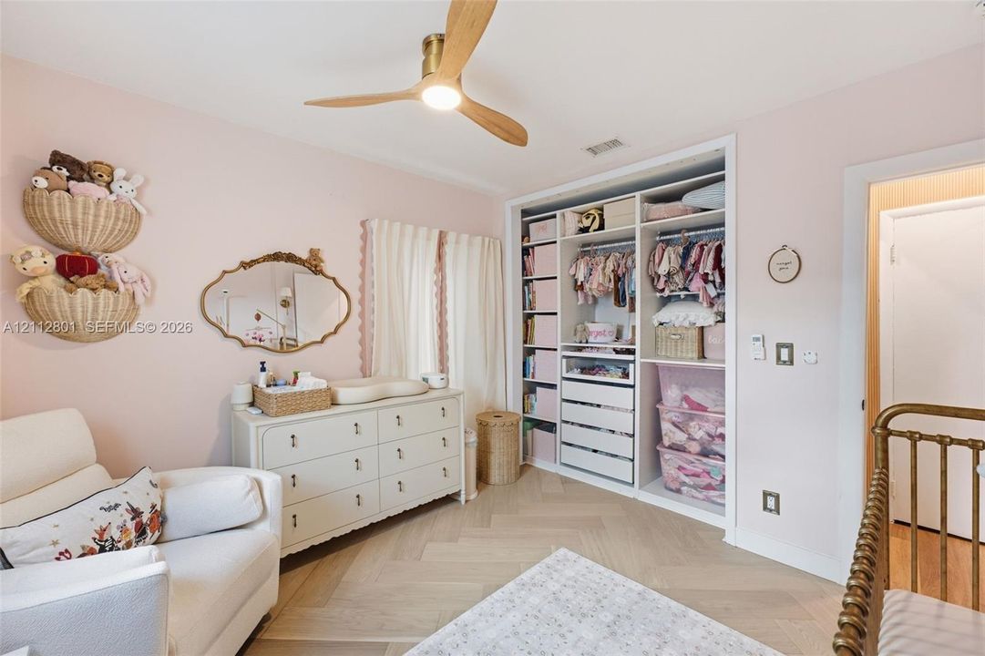 Custom built-in storage unit with open shelving and drawers, light-toned wood-finish flooring in a herringbone pattern, and a ceiling-mounted wooden-blade fan with integrated lighting