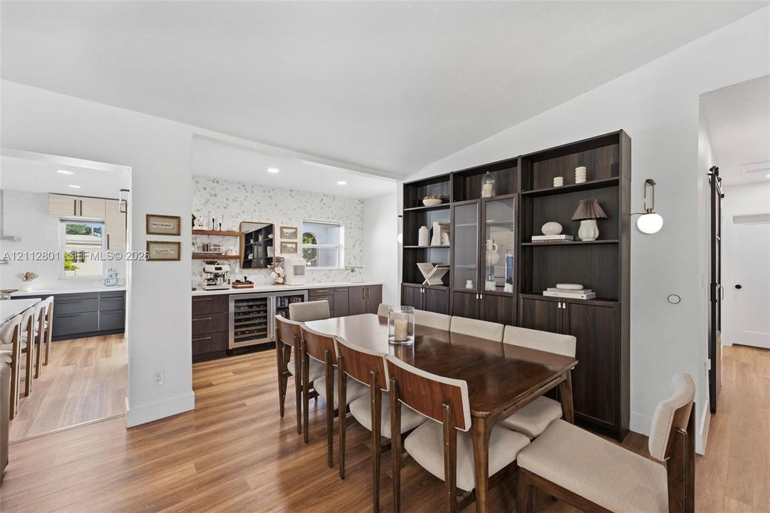 Wood-finish flooring, floor-to-ceiling dark wood built-in cabinetry, custom wet bar with under-counter refrigeration, recessed lighting, and modern wall-mounted light fixture