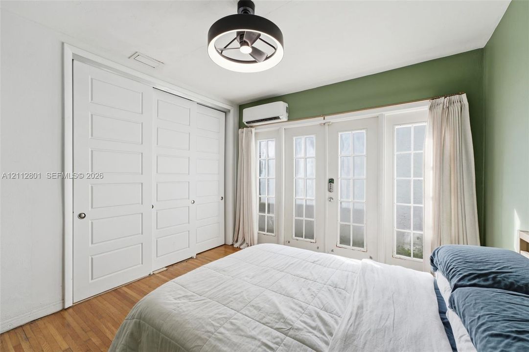 Room featuring wood-finish flooring, a wall-mounted ductless mini-split system, double glass-panel doors with grid detailing, and floor-to-ceiling built-in closet cabinetry