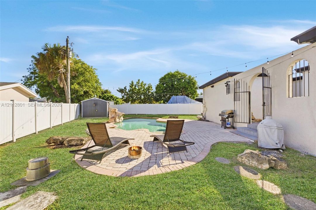 Backyard featuring a freeform swimming pool, decorative stone accents, paver patio, and white vinyl perimeter fencing