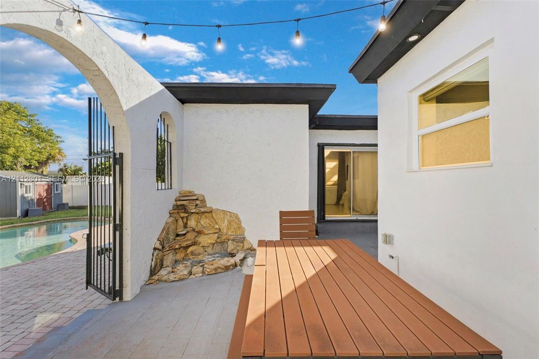 Outdoor patio featuring a built-in stone water feature, decorative arched entryway, and integrated overhead string lighting