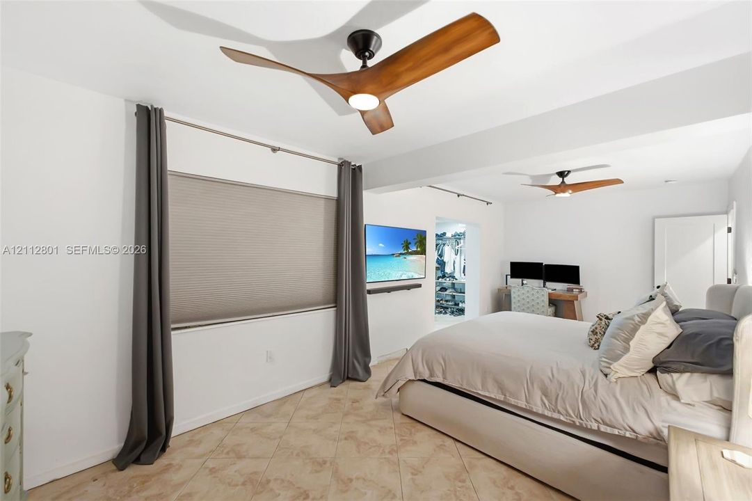 High-ceilinged room featuring two modern three-blade ceiling fans with integrated light kits, neutral tile flooring, and neutral wall-mounted cellular shades