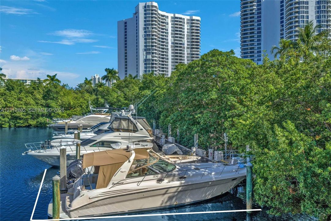 Deep-water boat slip featuring concrete pilings and direct waterway access, bordered by mature trees and established greenery