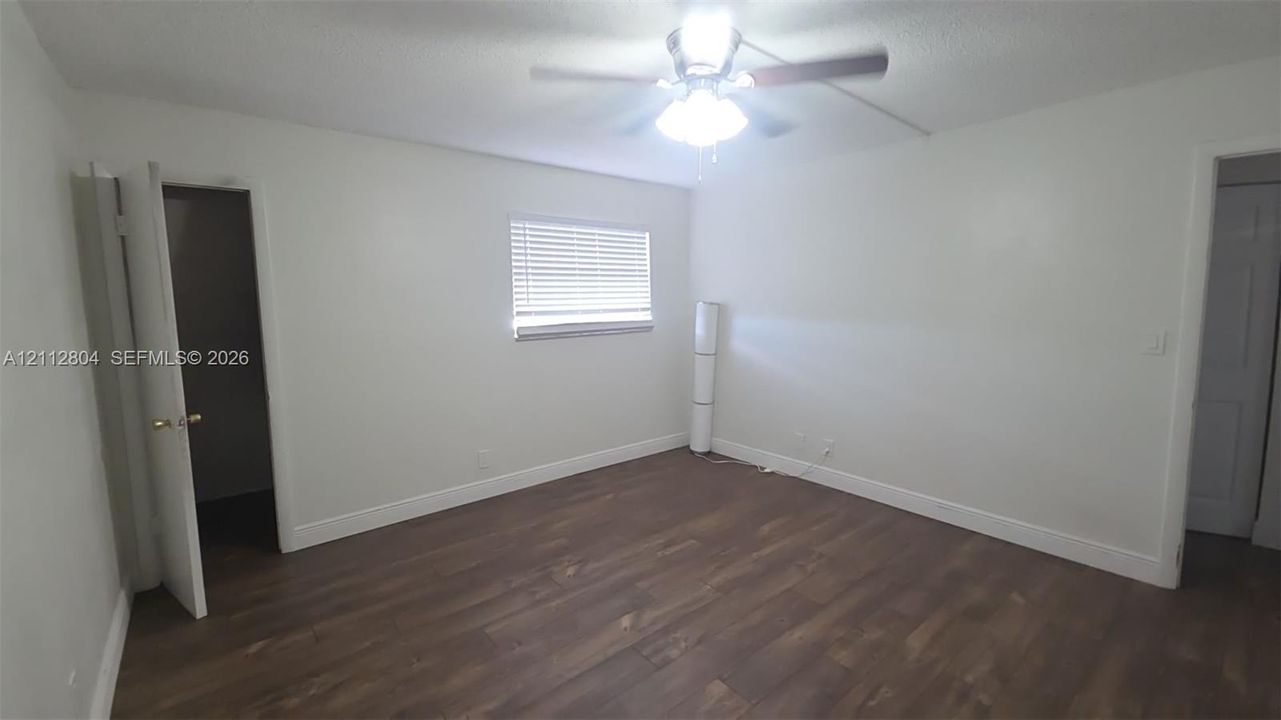 Room featuring dark wood-finish flooring, a ceiling fan with integrated lighting, and a window with horizontal blinds